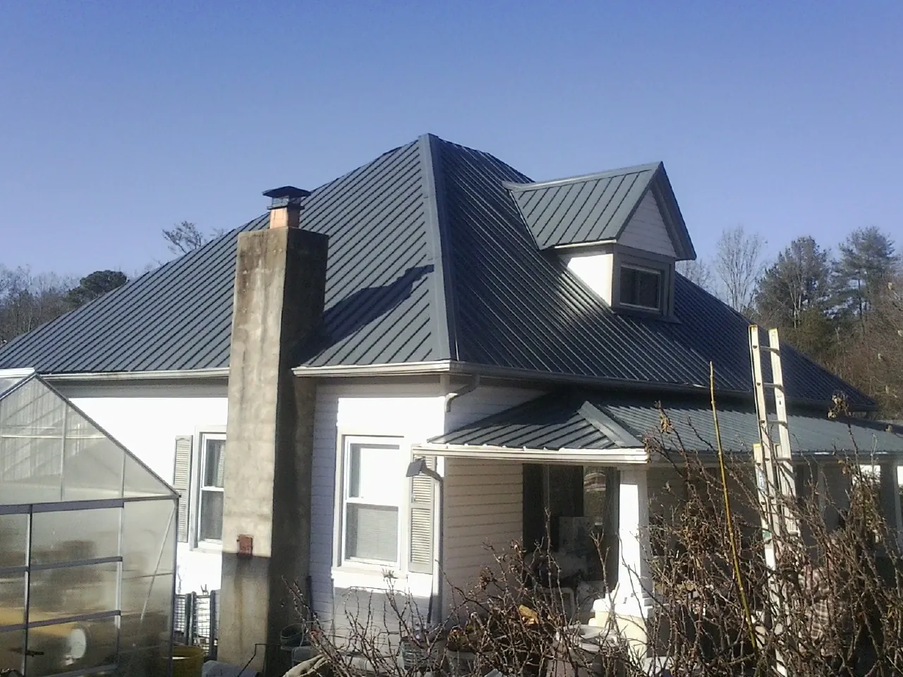 Dark blue standing seam metal roof on a white farmhouse with dormer — Slate & Tile Roof Repair by Roofing Brothers in Folcroft