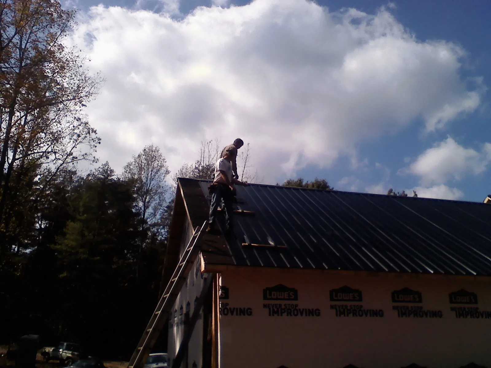 Roofer fastening dark metal panels high against a cloudy sky, from a Roof Inspection job in Folcroft