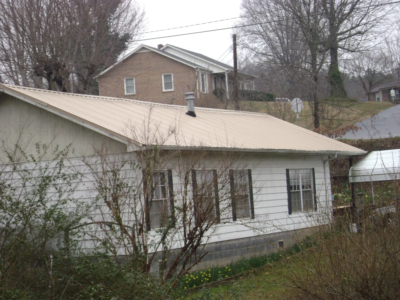 Tan metal roof on a white sided house set into a hillside — Commercial Roofing by Roofing Brothers in Folcroft